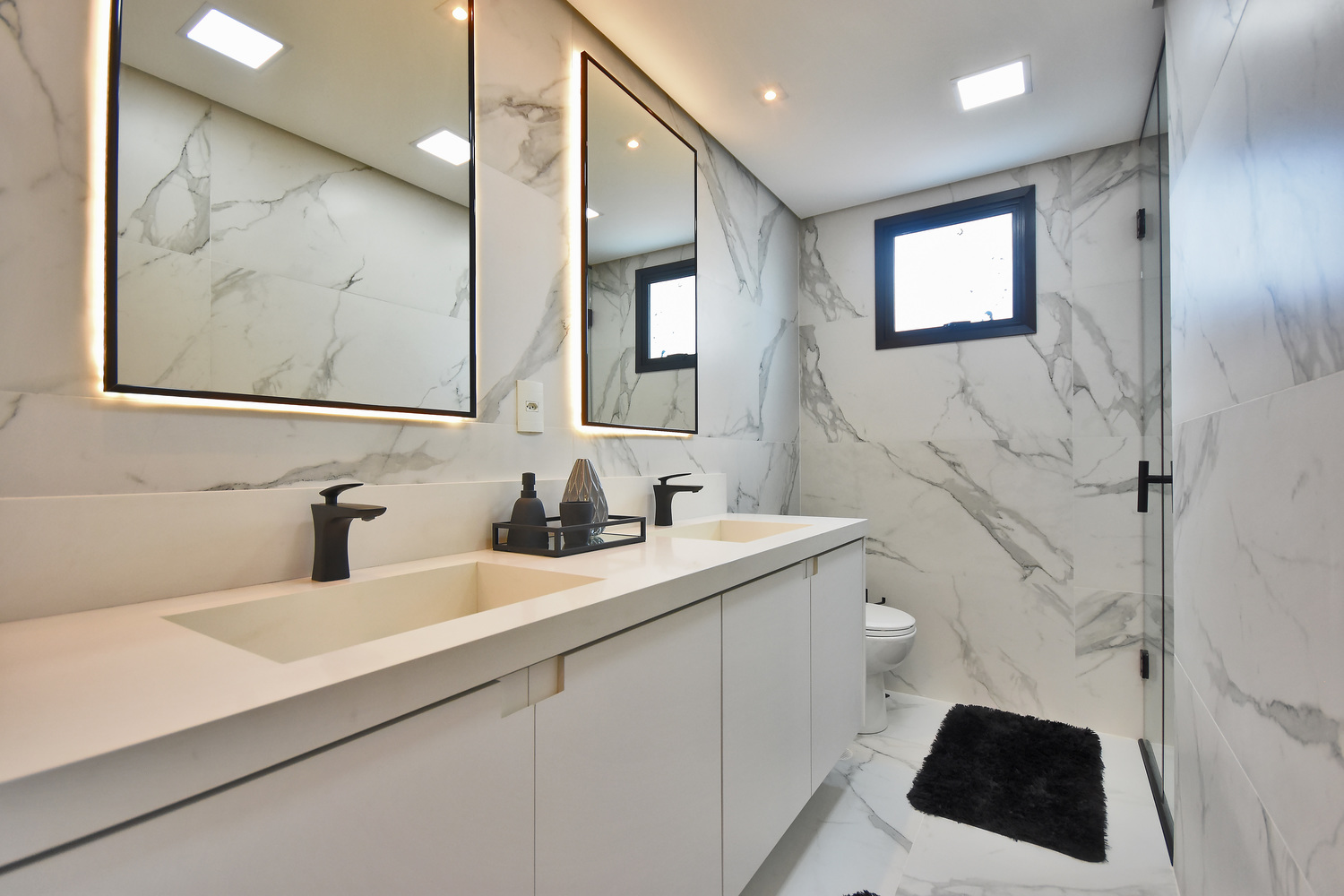 Banheiro da maior suíte do apartamento decorado do Residencial Piemonte.  Os espelhos, metais pretos e revestimentos marmorizados podem ser adquiridos pelos  projetos de personalização.